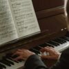 Close-up of a man playing a piano, focusing on hands and sheet music indoors.