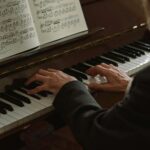 Close-up of a man playing a piano, focusing on hands and sheet music indoors.