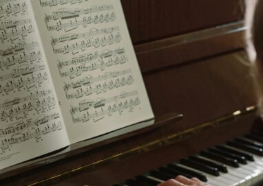 Close-up of a man playing a piano, focusing on hands and sheet music indoors.