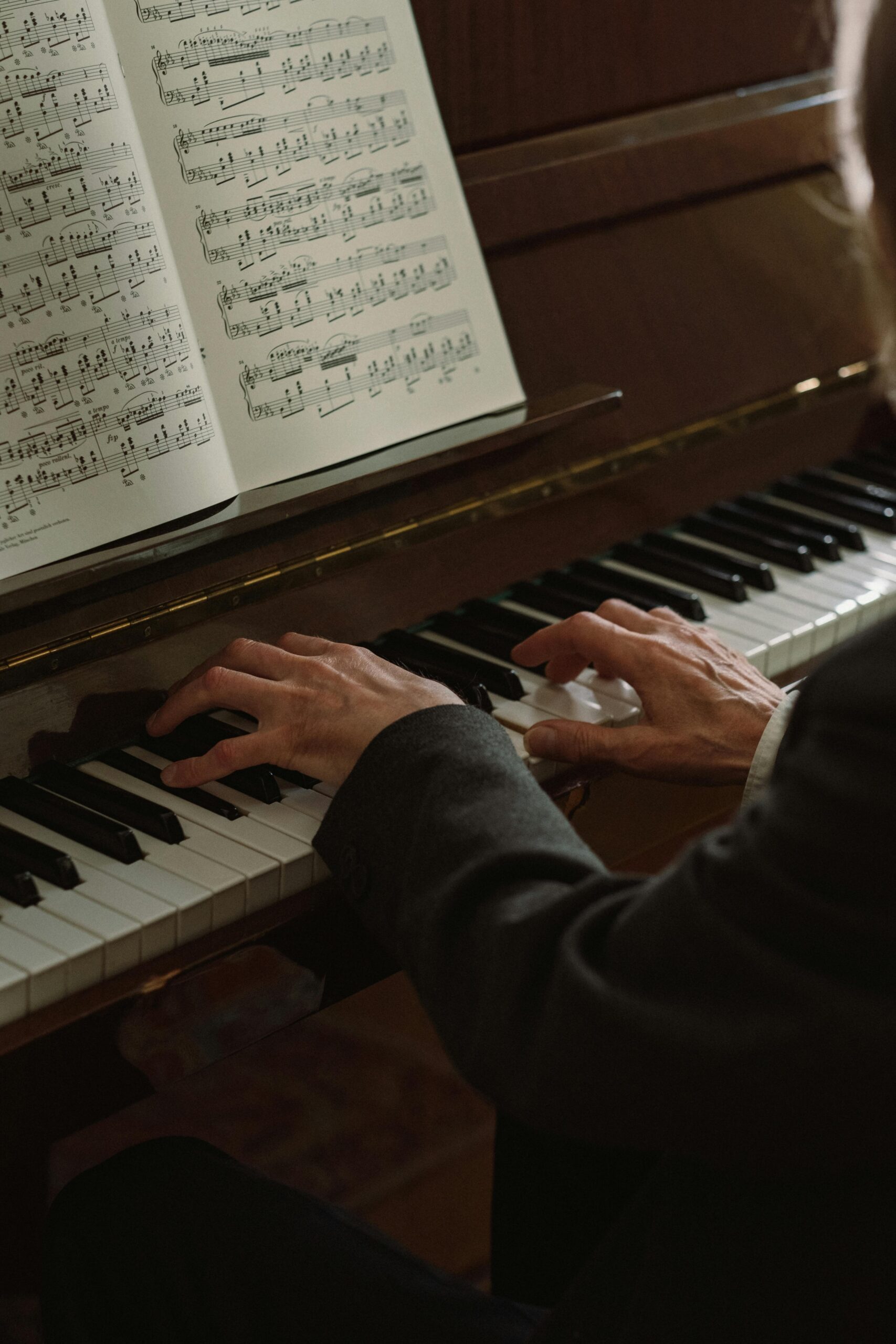 Close-up of a man playing a piano, focusing on hands and sheet music indoors.