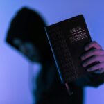 A hooded figure holds a Bible in low-light setting, emphasizing spirituality and mystery.